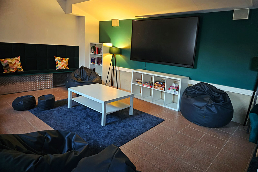 Strefa relaksu z pufami, kanapami, dużym telewizorem i innymi meblami.