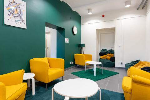 Przestrzeń w zielono-żółtych kolorach, z fotelami, stolikami i pufami.