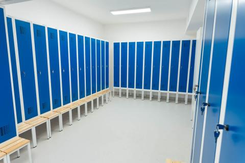 Pomieszczenie z wysokimi szafkami z niebieskimi drzwiami i jasnymi ławkami przy każdej szafce.